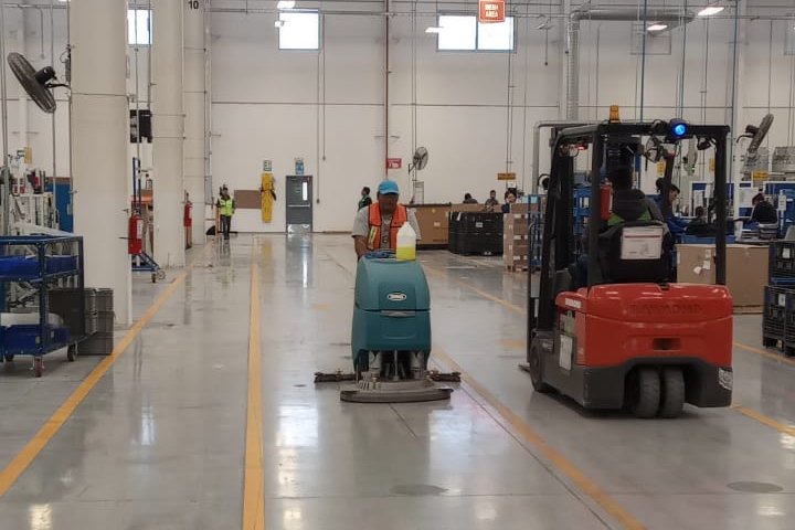 Fregadora en operación dentro de una planta industrial, junto a un montacargas